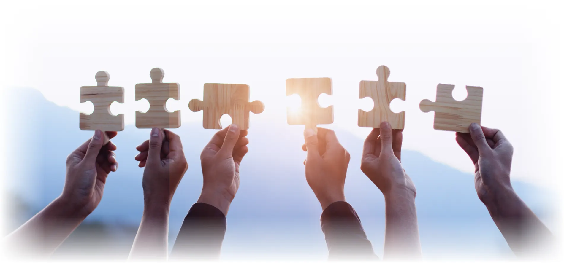 Several hands each holding a puzzle piece up to the light, coming together — the connected pieces of coordinated workers' compensation behavioral health